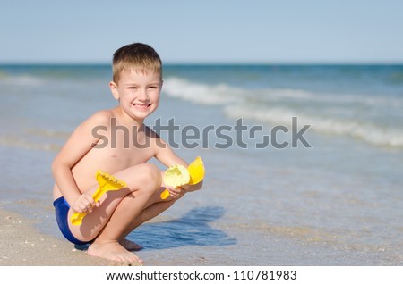 The nice smiling boy playing toys on the seashore