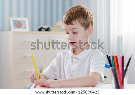 Young cute boy draws with color pencils in the children\'s room
