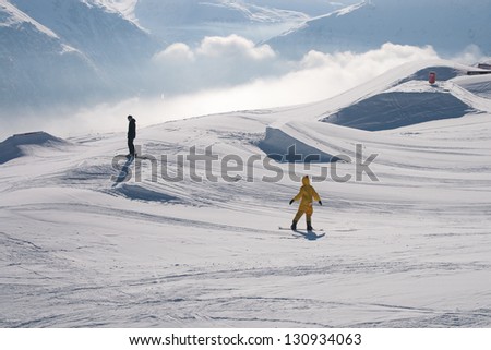 Snowboarder in bright yellow chicken costume preparing to jump, in a resort in the Alps