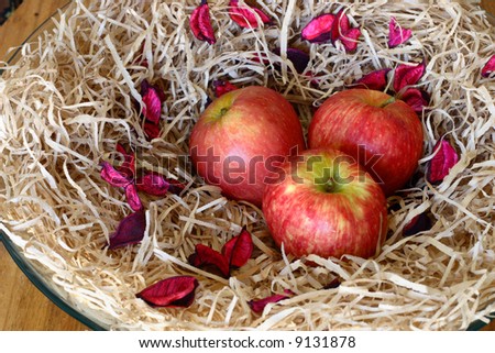 Three apples on a background of petals of colors in a decorative vase on a wooden table