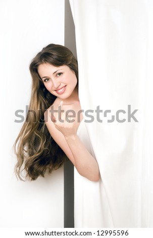 Beautiful young woman looking from behind a white curtain