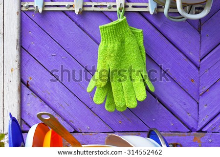 Green gloves against violet boards. A hanger on a wall of the private house. Abstract symbol of homestead economy.
