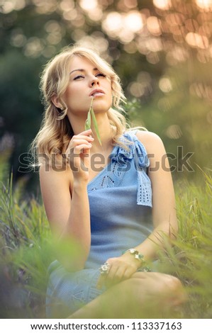 Girl sitting in the grass with a blade of grass in his mouth
