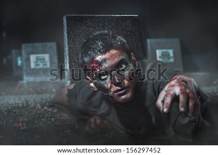 scary zombie crawls out of the grave at the cemetery