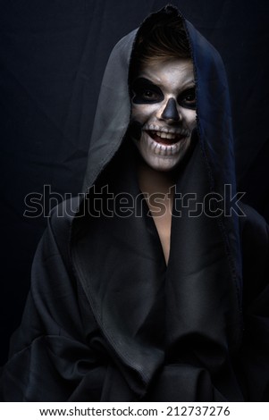 Teen with make-up of the skull in a black cloak laughs