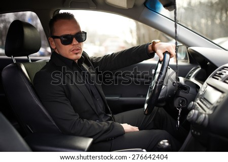 man in a black suit sitting behind the wheel