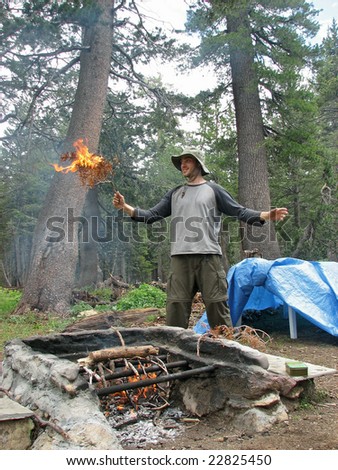 A hiker holding a burning branch above an outdoor fire place in the Sierra Neavada Mountains.