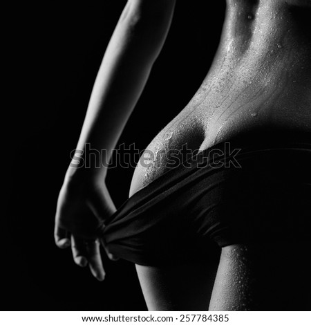 Black and white sexy female ass with perfect muscles in black sportswear and drip drops of water on black background