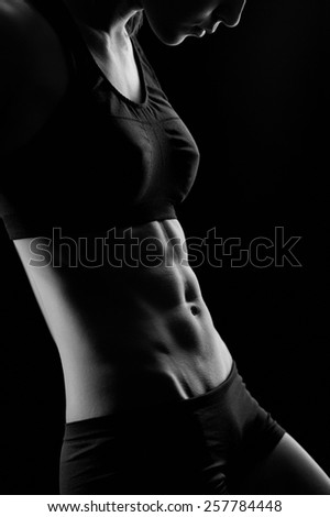 Black and white sporty sexy girl with great abdominal muscles in black sportswear and drip drops of water on black background