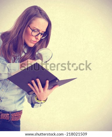 young girl holding a book looking through a magnifying glass