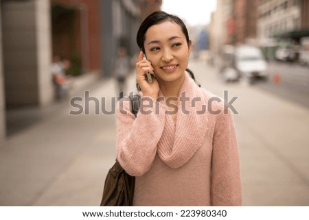 Young Asian Woman walking talking on cellphone on city street