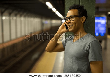 Young African Asian man in New York City in subway station talking on cell phone
