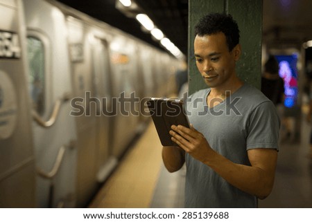 Young African Asian man in New York City in subway station using tablet pc