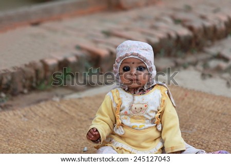 GODAWARI, NEPAL - OCTOBER 15: Eye painted unidentified little baby sits on a mat at the entrance to an old newar style house in a street of Godawari. Lalitpur distr.-Bagmati zone-Nepal.