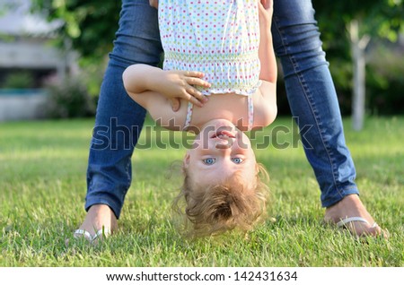 Mother holding her little girl upside down in the garden