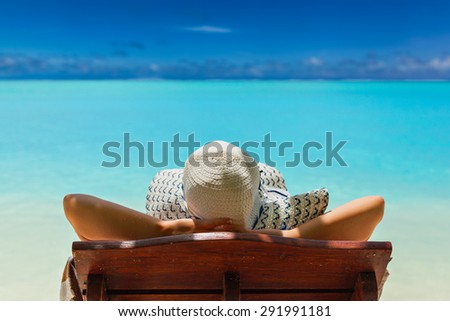 girl lays on a chaise lounge in the back on the banks of the turquoise Caribbean sea on Bahamian Maldivian Hawaiian beaches