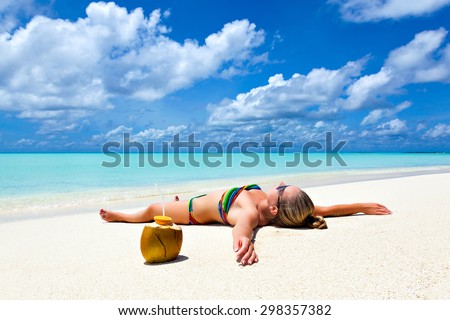 Young tanned woman girl lies on the beach with coconut on white sand by the tropical turquoise waters of the Caribbean to Hawaii Maldivian resort