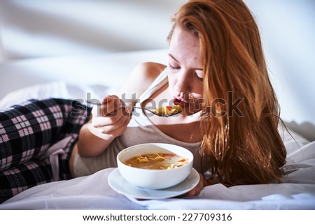 in bed eating chicken noodle soup while sick