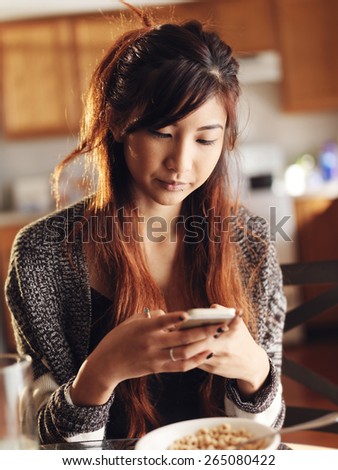 asian girl using smart phone in kitchen at breakfast