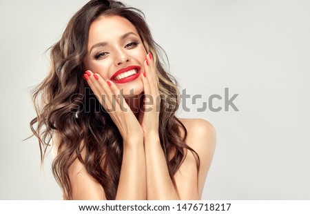 Beautiful laughing brunette model  girl  with long curly  hair . Smiling  woman hairstyle wavy curls . Red  lips and  nails manicure .    Fashion , beauty and make up portrait
