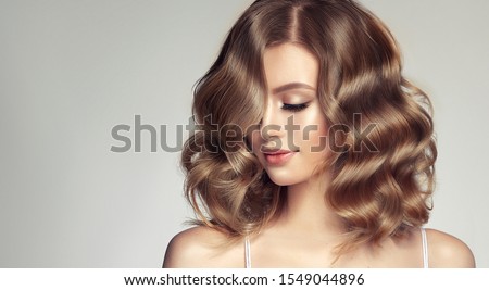 Woman with curly beautiful hair  on gray background. Girl with beauty a pleasant smile. Short wavy  hairstyle