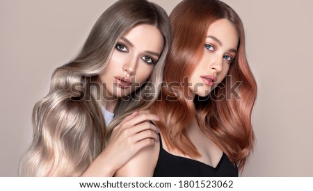 Beautiful women with curly hair.Two pretty girls with hair coloring in red and  shatush techniques. Stylish hairstyle curls done in a beauty salon. Fashion, cosmetics and makeup.