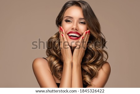 Beautiful laughing brunette model  girl  with long curly  hair . Smiling  woman hairstyle wavy curls . Red  lips and  nails manicure .    Fashion , beauty and make up portrait