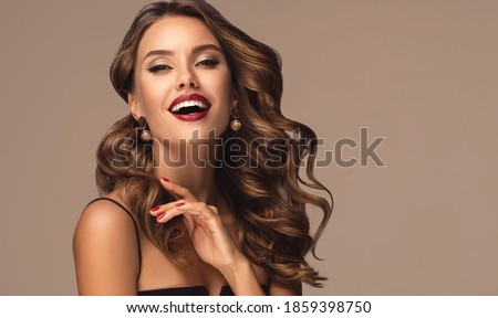 Beautiful smiling woman with long wavy hair .  Girl curly hairstyle  and red manicure nails . Beauty ,makeup and cosmetics . Earring jewelry