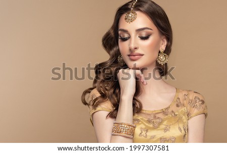 Portrait of beautiful indian girl. Young hindu woman model with golden kundan jewelry set, earrings, tikka and bracelet  . Traditional India costume lehenga choli or saree . Curly hair