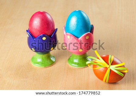 Colored easter eggs in egg cups on wooden table, focus on the foreground