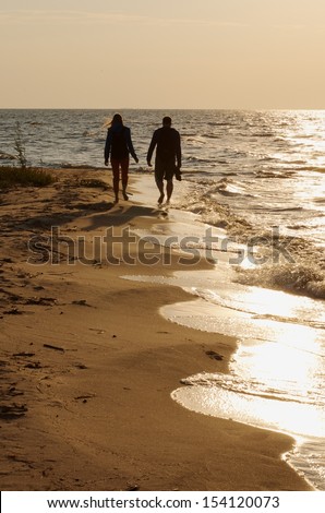 Silhouette of walking young couple by the sea on golden sunset with the calm sea background, multicolored sunset and man and woman walking near the sea, two people in love in sunset time, lovers