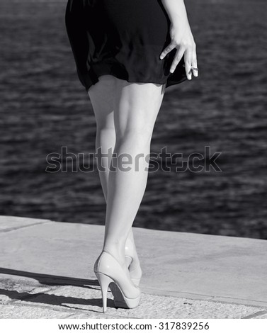 Isolated sexy elegant woman\'s legs with high heels in blurry natural background, body part fragment, woman standing near the sea in black and white photo
