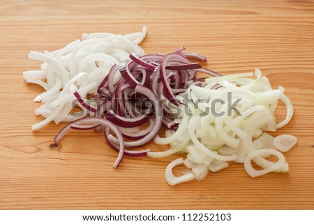 White, red and yellow onion rings on a wooden board