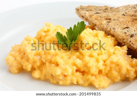 Soft scrambled eggs with parsley next to brown toast on a white plate.