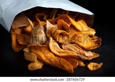 Open packet of fried parsnip and carrot chips on black.