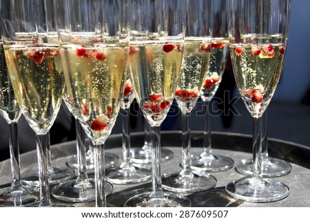 Sparkling champagne flutes on tray with pomegranate seeds.