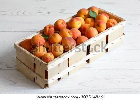 Wood box of whole orange apricots with red blush on rustic white wood. Space for text.