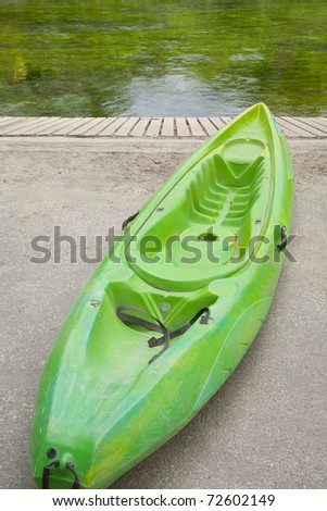 Green kayak on shore next to the green water of a stream.