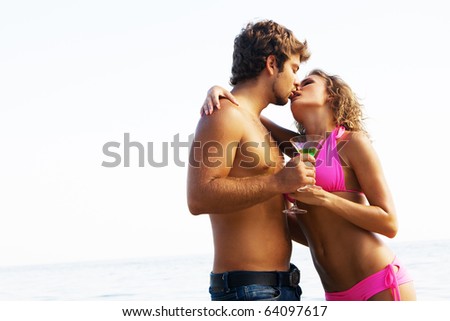 Young couple on the seaside with exotic cocktails is passionately kissing