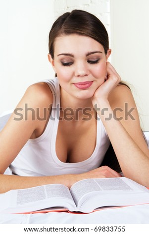 Young beautiful woman reading a book in bed