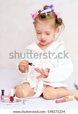 little girl painting nails while wearing hair-rollers, at home
