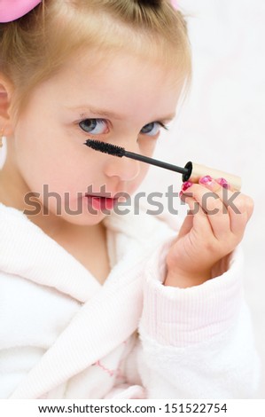 little girl painting eyes while wearing hair-rollers and bathrobe