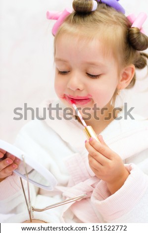 little girl painting lips while wearing hair-rollers and bathrobe