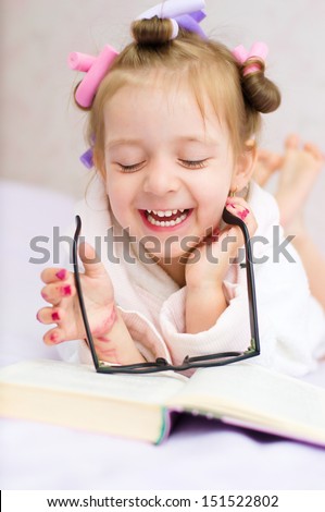 little girl is playing with book and glasses, while wearing hair-rollers and bathrobe