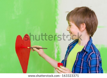 cute boy painting red heart on the wall at home