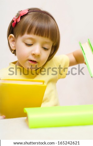 Cute little girl play with books while sitting at table