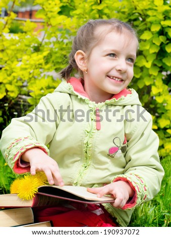 spring portrait of a cute little girl reading a book outdoors