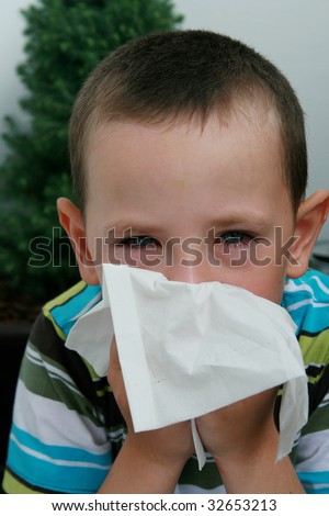 Five years old boy with tissue blowing his nose. Child with allergy, conjunctivitis and black rings round his eyes.