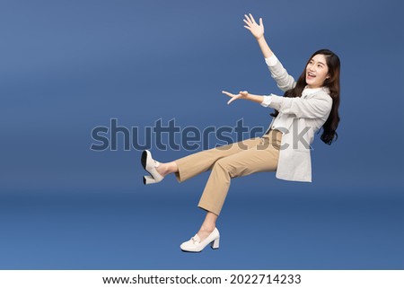 Happy cheerful young Asian businesswoman in suit floating in the air isolated on blue background, Presentation concept