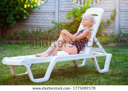 A beautiful girl of 6-7 years old in a bathing suit lies on a deck chair in the garden, in the yard, on vacation with her eyes closed and a pacified expression on her face. Relaxation and meditation o Foto stock © 